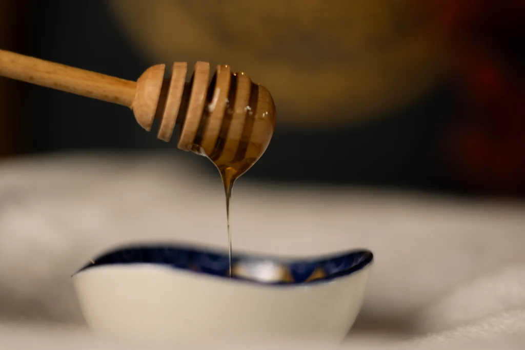 Naturalny miód pszczeli spływający z drewnianego czerpaka do miseczki – przygotowanie do masażu miodem w Viva Soma Karpacz.
